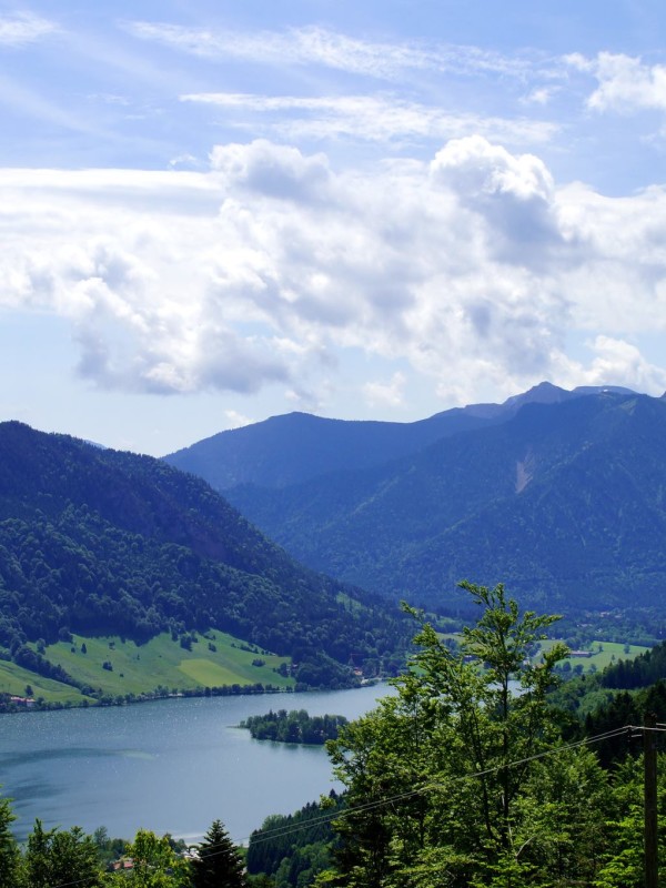 Der zauberhafte Blick auf den Schliersee in Alleinlage auf über 1.100 Meter. Der Schliersee zeigt sich vor Bergpanorama im weiß-blauen Himmel.