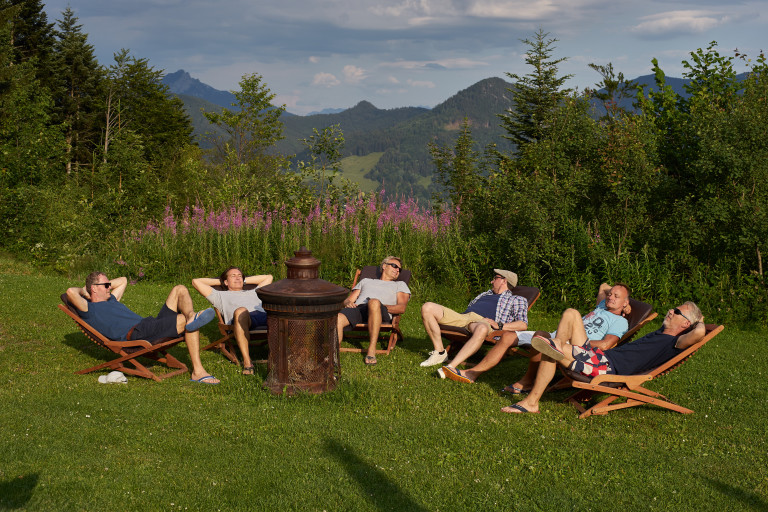 Freunde entspannen im Liegestuhl-Stuhlkreis vor dem sagenhaften Blick auf den Schliersee am Almbad Huberspitz