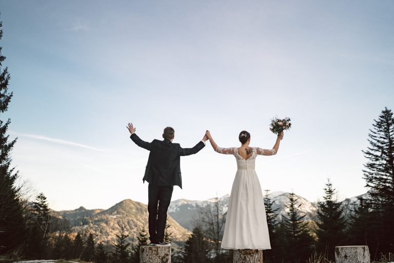 Das Brautpaar Hand in Hand jubelnd zu den Bergen